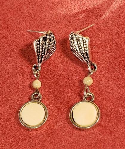 These unique Silver colored Fossil Mammoth Ivory Earrings are about 10,000 years old and made from ivory found in Alaska. The white mammoth ivory beads are from ivory found in Siberia. They are highlighted with hypo allergenic seashell ear posts. These earrings are a beautiful way to show off a piece of history. Their unique design is sure to turn heads and add a touch of timeless elegance to your wardrobe.